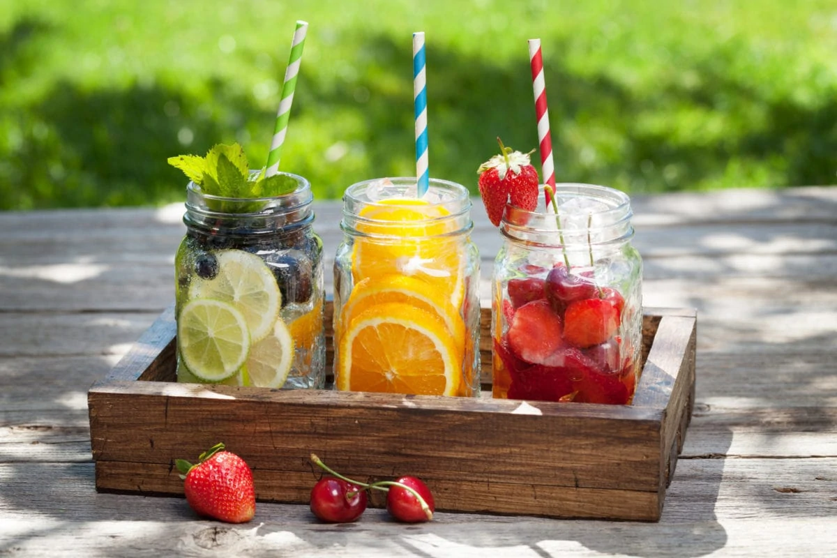 Three jars of fruit drinks with straws in a wooden box